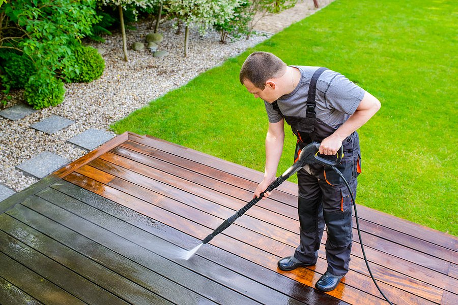 power washing - man cleaning terrace with a power washer - high water pressure cleaner on wooden terrace surface